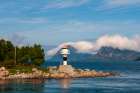 A lighthouse perches on a rocky promontory and reflects on Holandsfjorden Svartisen-Norway Art Print